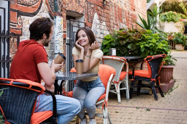 Donna sorridente che parla con fidanzato con tazza di carta sulla terrazza del caffè — Foto stock