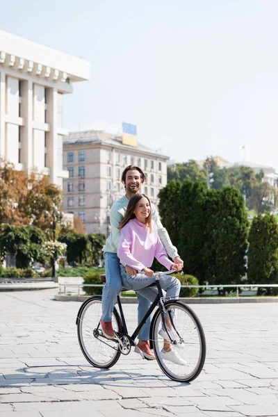 Счастливый мужчина ехал на велосипеде с подругой по городской улице в дневное время — стоковое фото