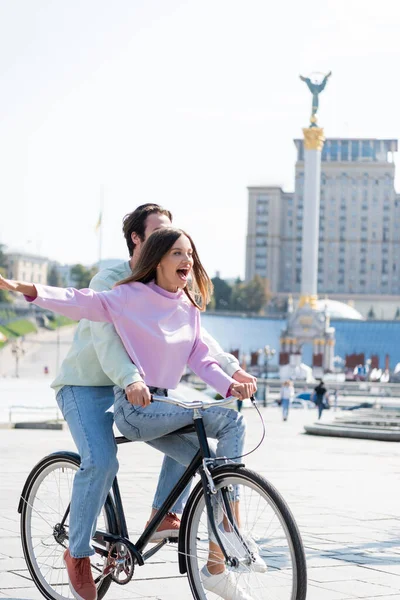 KYIV, UCRANIA - 1 de septiembre de 2021: Emocionada mujer montando en bicicleta con su novio en la Plaza de la Independencia - foto de stock