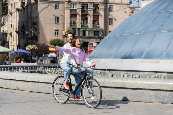 Glücklicher Mann radelt mit aufgeregter Freundin auf Stadtstraße — Stockfoto