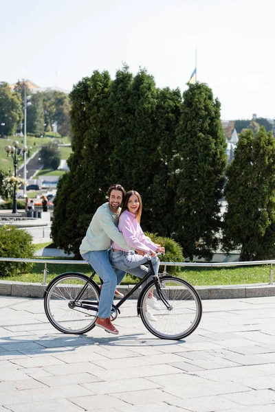 Happy couple riding bicycle and looking away on urban street — Stock Photo