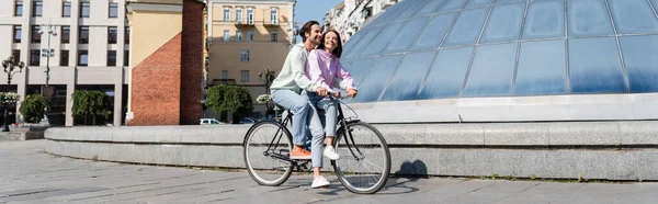 Mujer morena en bicicleta con novio sonriente en la calle urbana, pancarta - foto de stock