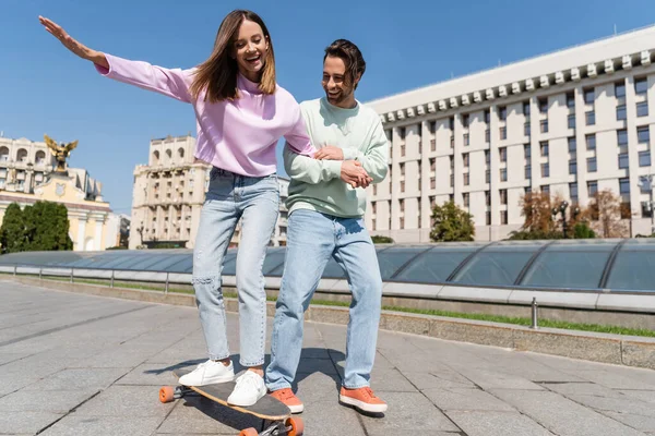 Positive couple riding penny board on urban street — Stock Photo
