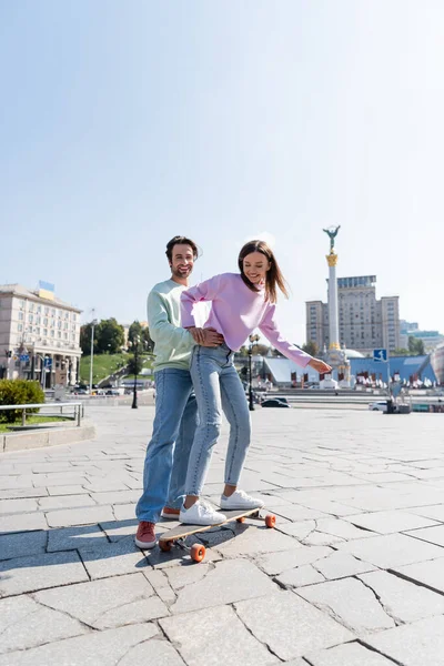 KYIV, UKRAINE - SEPTEMBER 1, 2021: Happy man hugging girlfriend riding penny board on urban street in Kyiv — Stock Photo