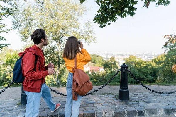 Tourist holding map near girlfriend with backpack and binoculars on urban street — Stock Photo