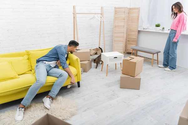 Young interracial couple looking at bengal cat near packages in living room — Stock Photo