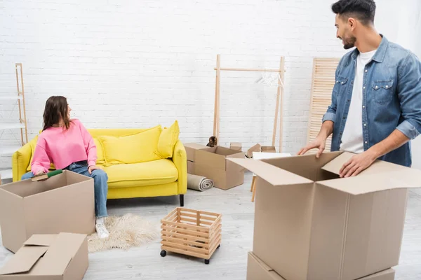 Smiling multiethnic couple looking at bengal cat while unpacking boxes at home — Stock Photo