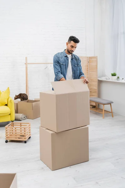 Muslimischer Mann packt Kartons neben Bengalkatze zu Hause aus — Stockfoto