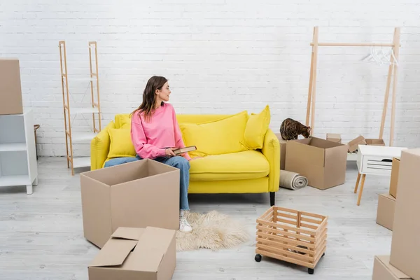 Vista lateral de la mujer sosteniendo libro cerca de bengala gato y cajas de cartón en casa - foto de stock