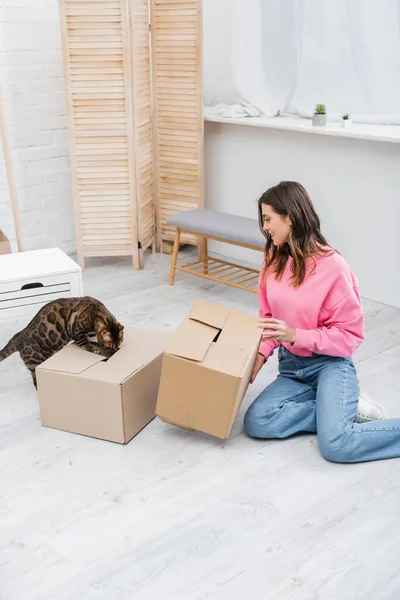 Side view of smiling woman holding cardboard box near bengal at at home — Foto stock