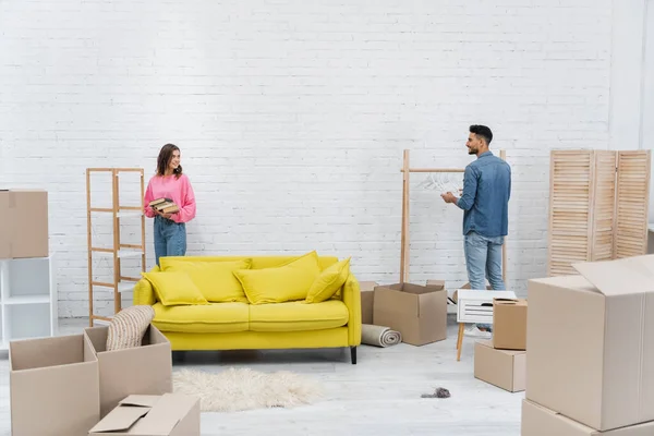 Cheerful multiethnic couple unpacking carton boxes in living room — Stock Photo