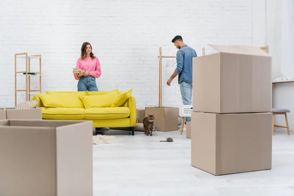 Cheerful interracial couple unpacking packages near bengal cat at home — Foto stock