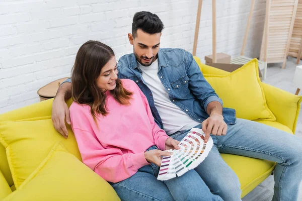 Arabian man pointing at color palette near girlfriend on couch at home — Photo de stock