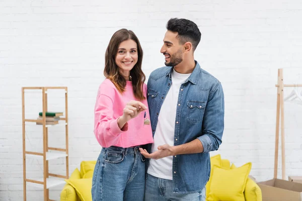 Cheerful woman holding key near arabian boyfriend at home - foto de stock