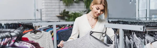 Young woman holding sweater on hanger in vintage shop, banner — Stock Photo