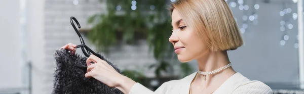 Vista laterale della donna bionda che tiene il maglione sul gancio nel negozio vintage, banner — Foto stock