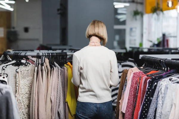 Вид ззаду жінки, що стоїть біля одягу в вінтажному магазині — стокове фото