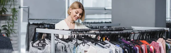 Happy woman loosing at clothes on hangers in second hand, banner — Foto stock