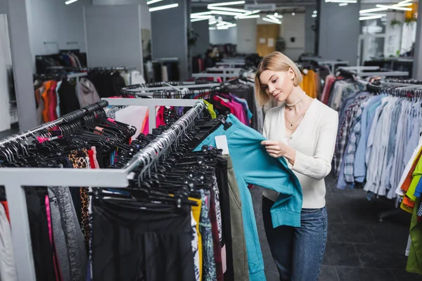Young blonde woman choosing pants in second hand — Photo de stock