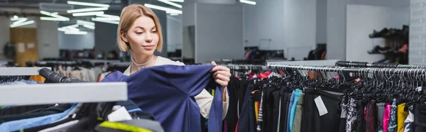 Pretty blonde woman choosing clothes near hangers in vintage shop, banner — стоковое фото