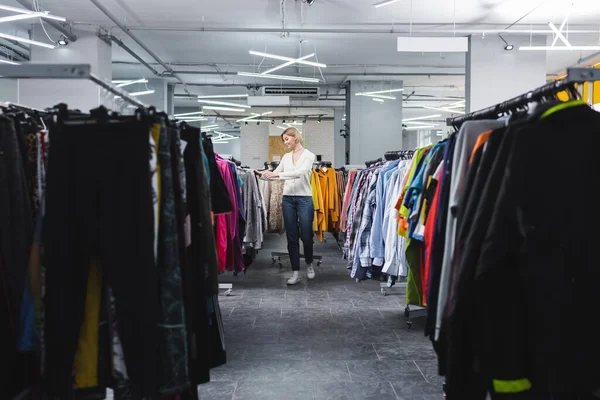 Vista lateral da mulher sorridente andando perto de roupas em segunda mão — Fotografia de Stock