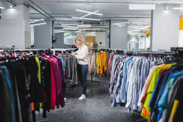 Side view of blonde woman taking hanger with clothes in vintage shop — стоковое фото