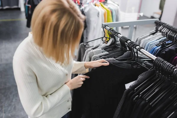 Mulher desfocada escolhendo roupas em cabides em segunda mão — Fotografia de Stock