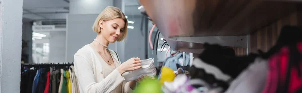 Blonde woman holding shoe near clothes in second hand, banner — Foto stock