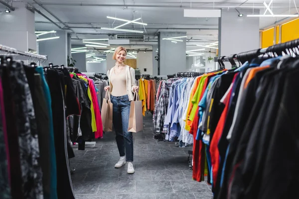 Mulher loira positiva segurando sacos de compras na loja vintage — Fotografia de Stock