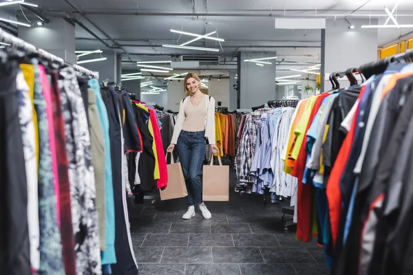 Smiling woman holding shopping bags and looking at camera in second hand — Foto stock