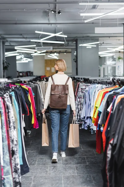 Vista lateral de la mujer joven sosteniendo bolsas de compras mientras camina en la tienda vintage - foto de stock