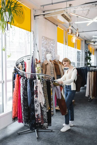 Smiling woman looking at scarfs on rack in vintage shop — Stockfoto