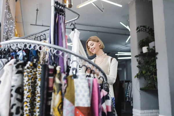 Low angle view of blonde woman choosing scarf in second hand — Photo de stock