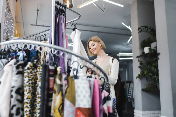 Low angle view of blonde woman choosing scarf in second hand — стоковое фото