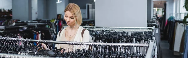 Young customer looking at hangers in second hand, banner — Stock Photo