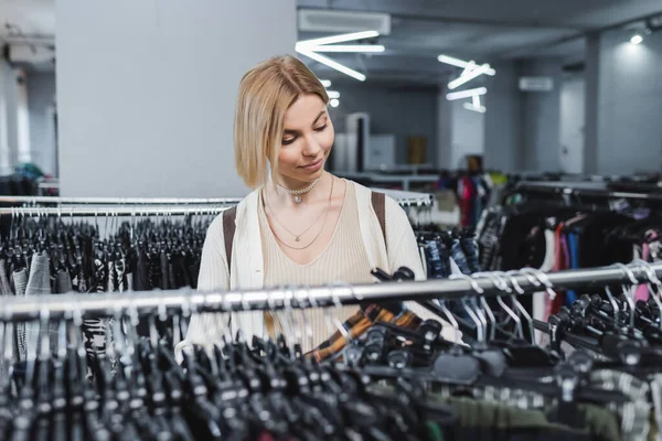Mujer joven mirando ropa borrosa en el estante en la tienda vintage - foto de stock