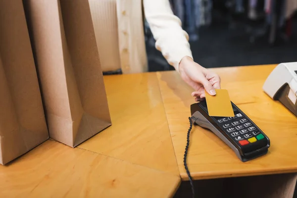 Vista recortada de una mujer borrosa pagando con tarjeta de crédito cerca de bolsas de compras en segunda mano - foto de stock