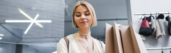 Blonde woman standing near shopping bags in second hand, banner - foto de stock