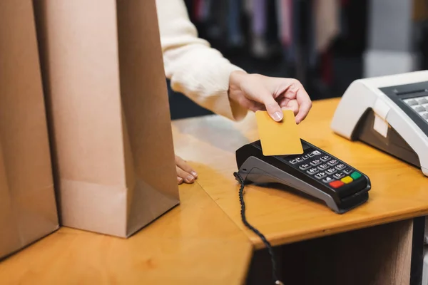 Vista cortada da mulher que paga com cartão de crédito perto do terminal de pagamento e sacos de compras em segunda mão — Fotografia de Stock