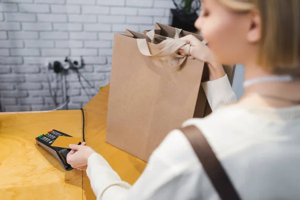 Mujer borrosa pagando con tarjeta de crédito y sosteniendo bolsas de compras en segunda mano - foto de stock