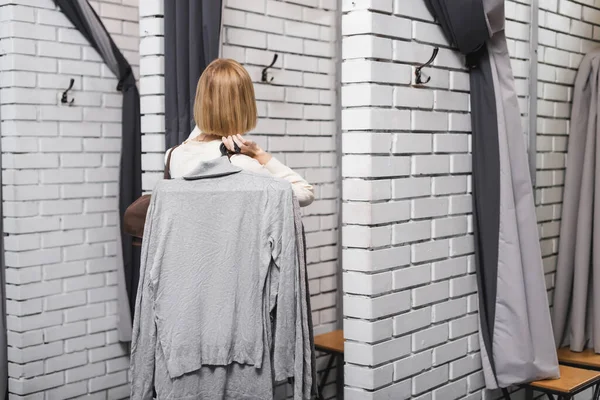 Back view of blonde woman holding hangers with cloth in second hand — Stockfoto