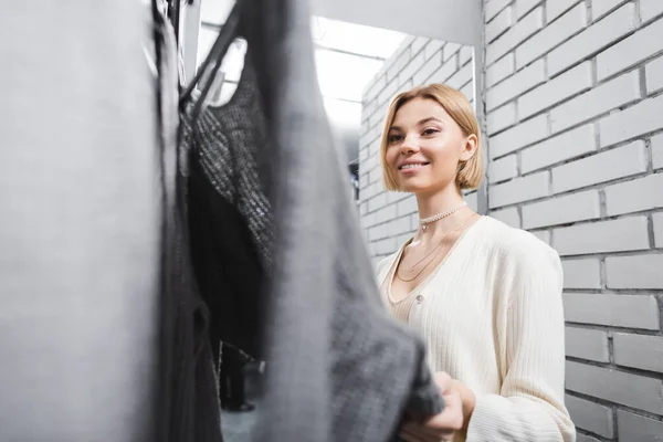 Mulher sorridente olhando para roupas em camarim em segunda mão — Fotografia de Stock