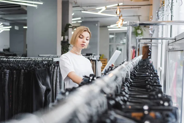 Saleswoman holding digital tablet near clothes on blurred rack in vintage shop - foto de stock