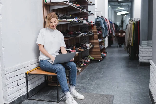 Vendedora joven usando portátil cerca de zapatos en tienda vintage - foto de stock