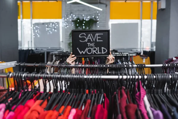 Vue recadrée du panneau de maintien du détaillant avec sauver le monde lettrage près de vêtements d'occasion — Photo de stock