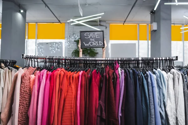 Vista recortada del tablero de contención minorista con letras salvar el mundo cerca de la ropa en la tienda vintage - foto de stock