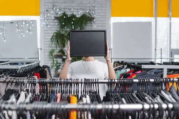 Saleswoman holding board near clothing in second hand — Photo de stock