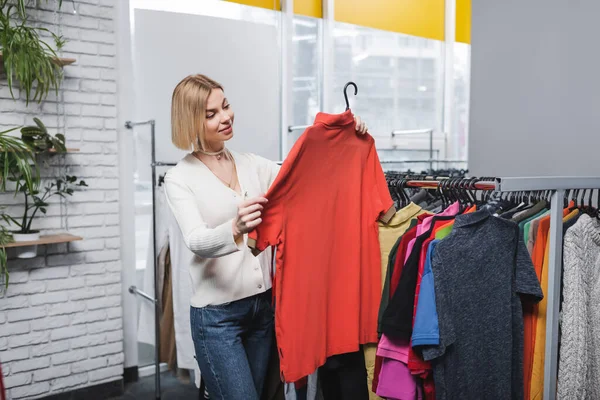 Happy blonde customer looking at t-shirt in retro store — Stock Photo