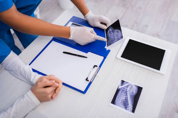 Vista recortada del médico afroamericano apuntando a ecografía cerca de colega y tableta digital en clínica - foto de stock