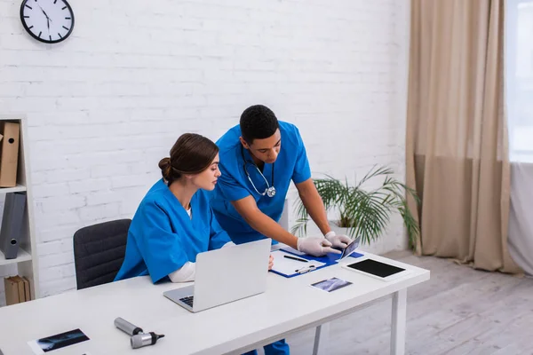 Interracial vet doctors looking at ultrasound scan near devices in clinic — Photo de stock